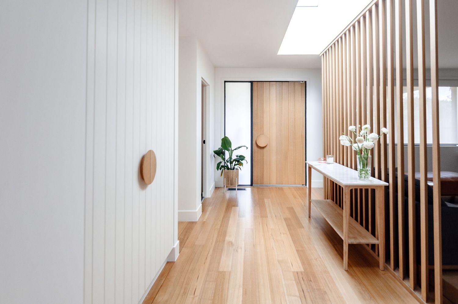 Light-filled hallway with wooden floors, white walls, and vertical slat room divider.