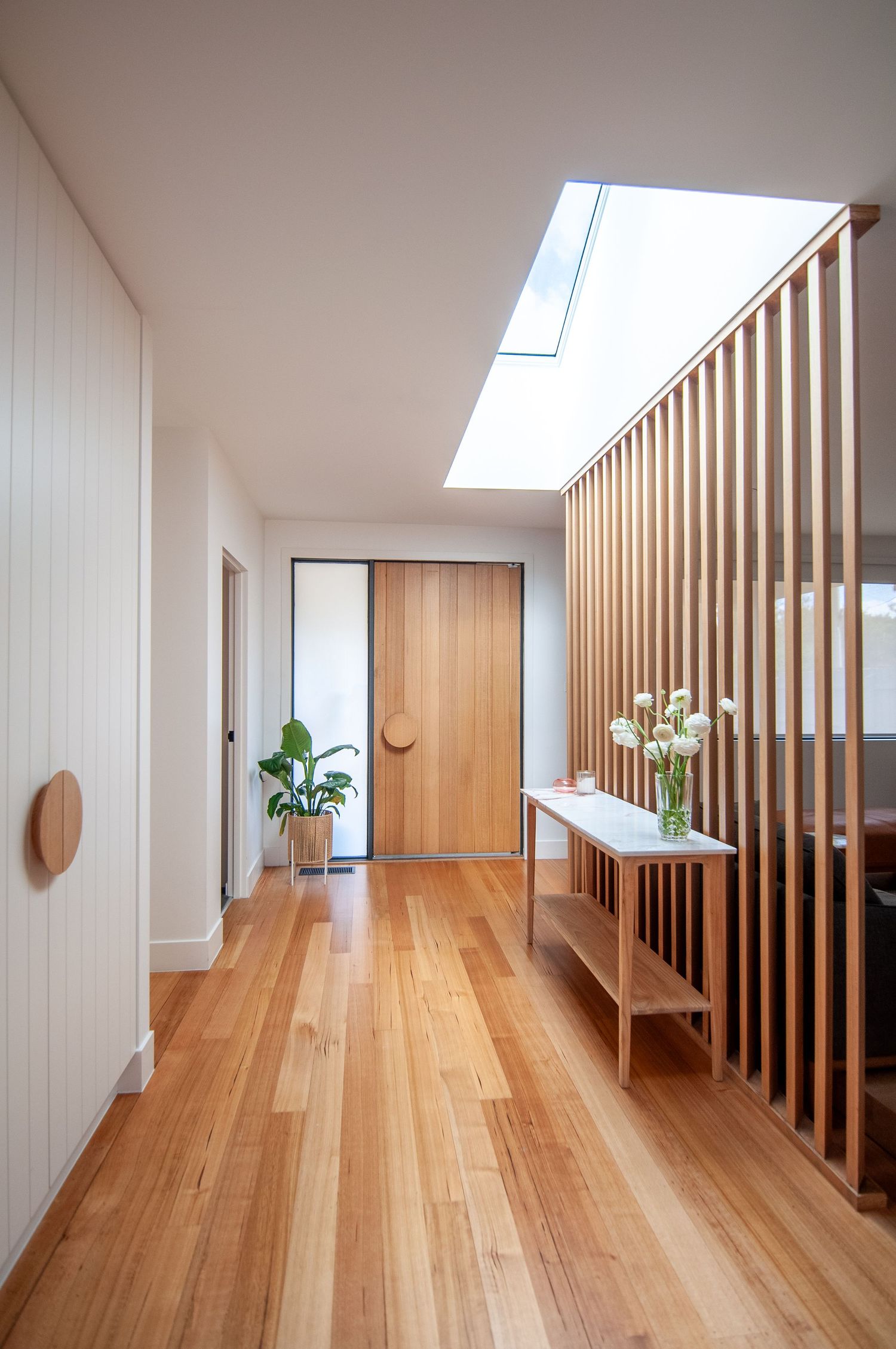Bright hallway with wooden slat divider, skylight, and hardwood flooring showcasing minimalist design elements.