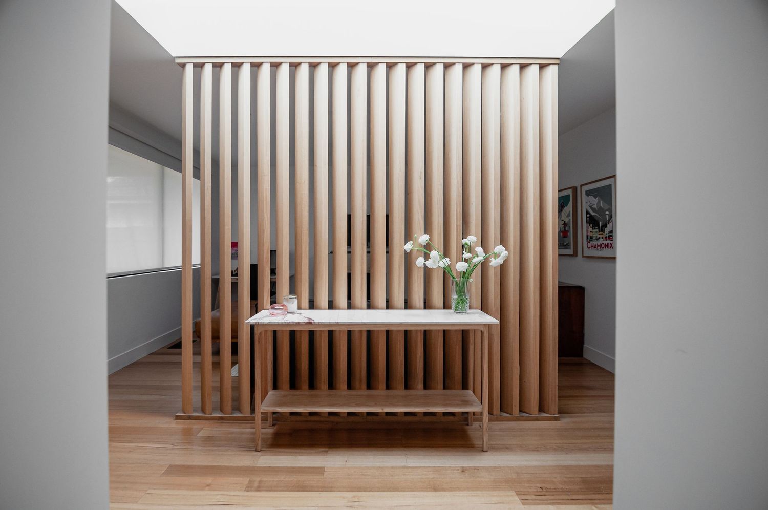 Architectural detail of wooden slat room divider with floating console table and decorative white flowers.