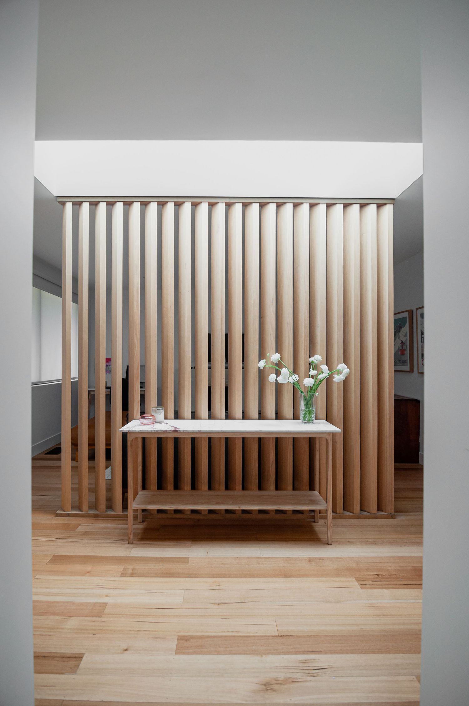 Modern entryway featuring vertical wooden slats dividing the space with a minimalist console table and white flowers.