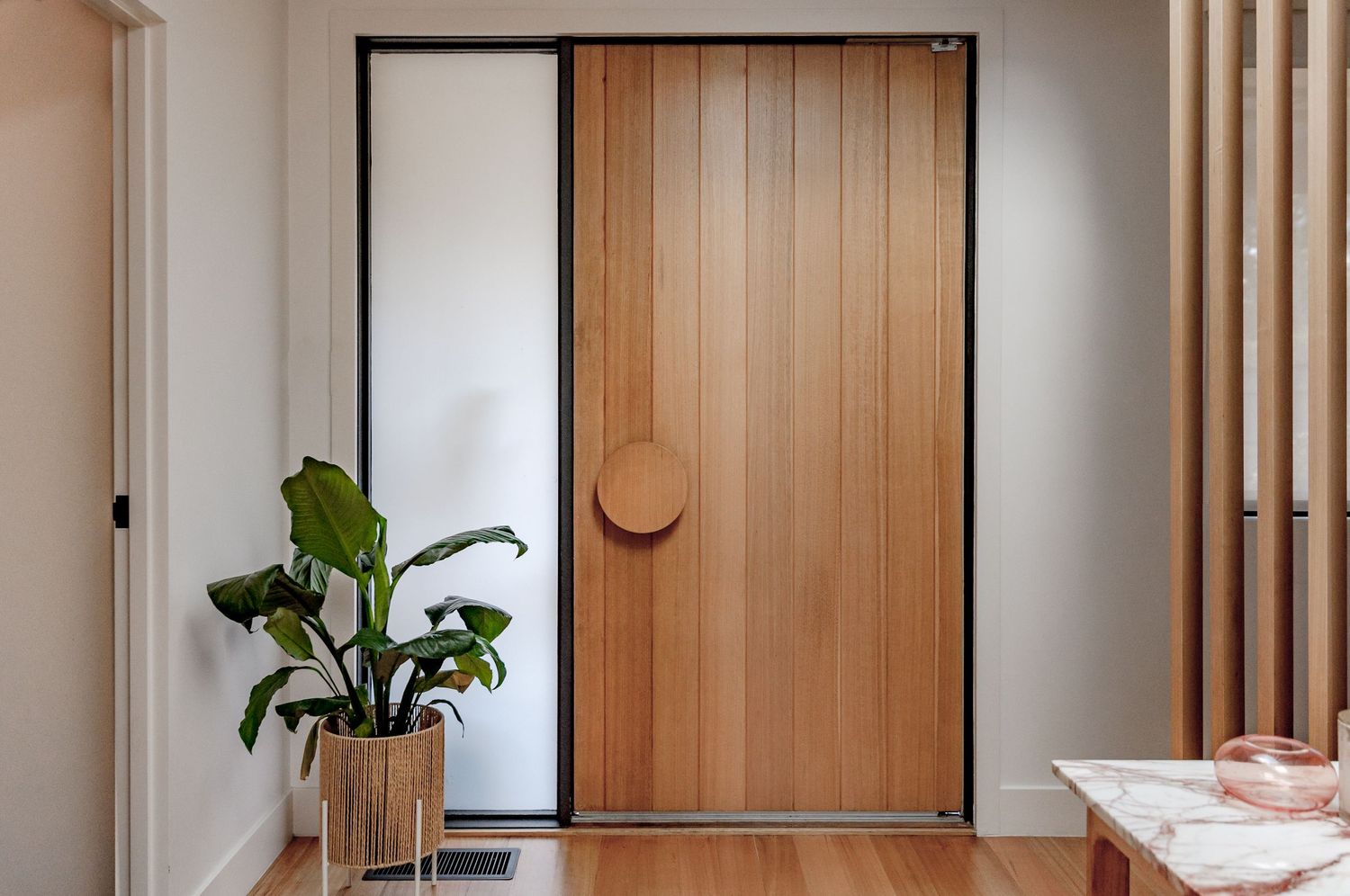 Modern wooden front door with circular handle and potted plant creating a welcoming entrance.