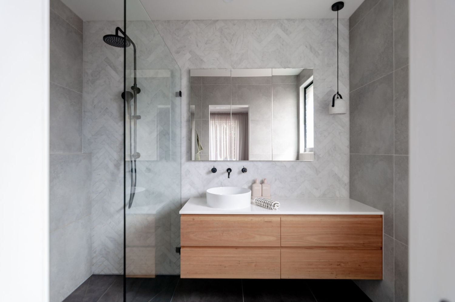 Contemporary bathroom with floating wooden vanity, marble-look walls, and modern shower fixtures.