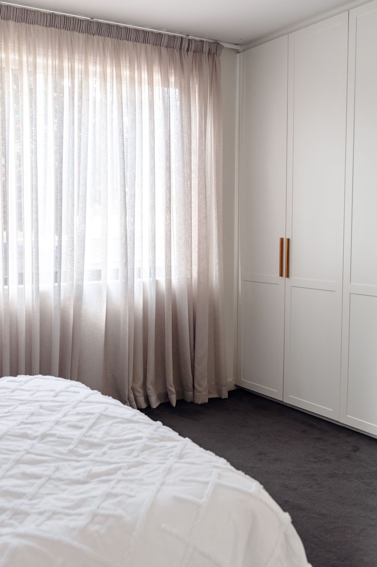 Serene bedroom interior with white built-in wardrobes and sheer curtains filtering natural light.