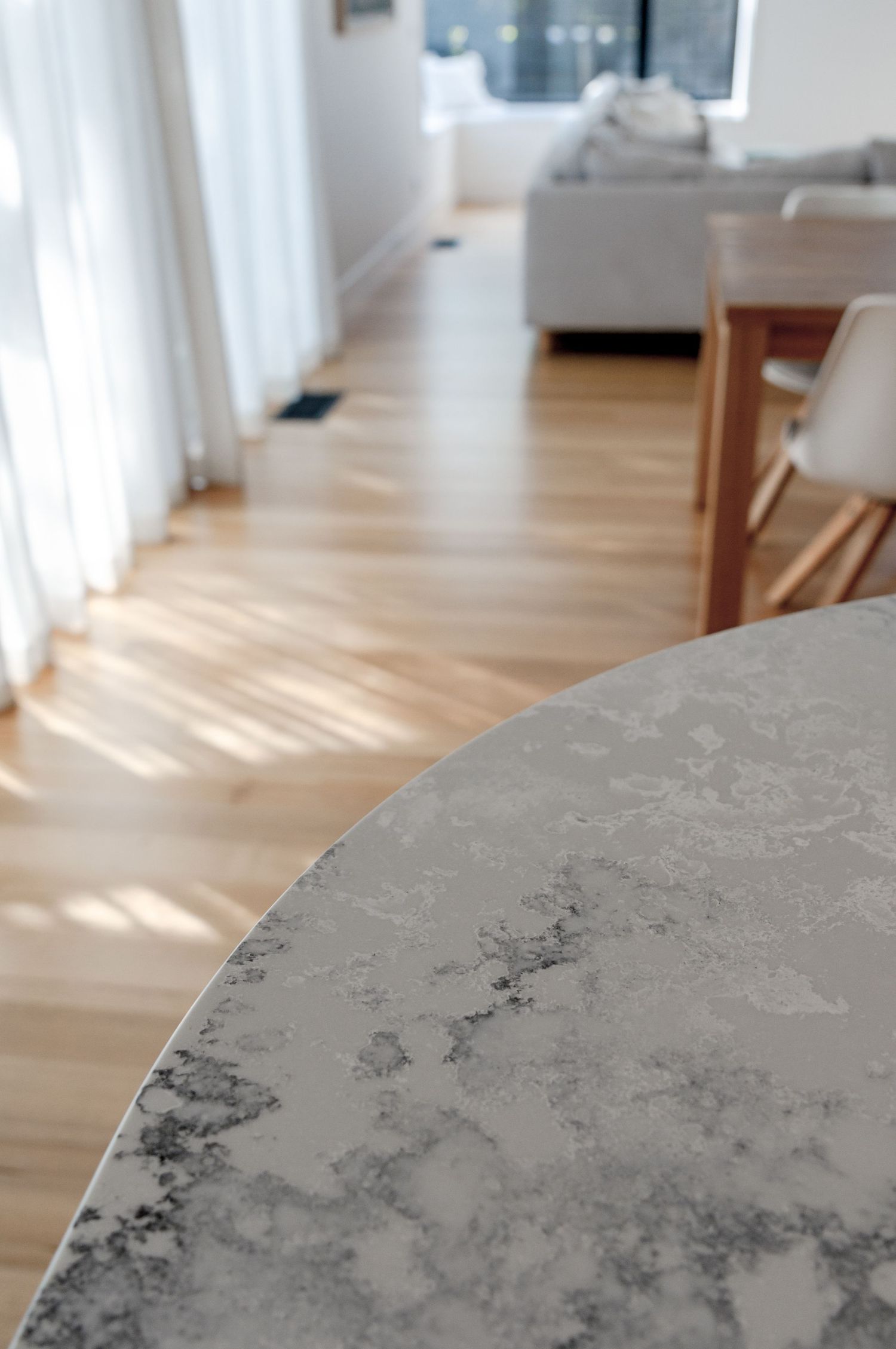 Close-up of marble table surface with hardwood flooring and sheer curtains in background.