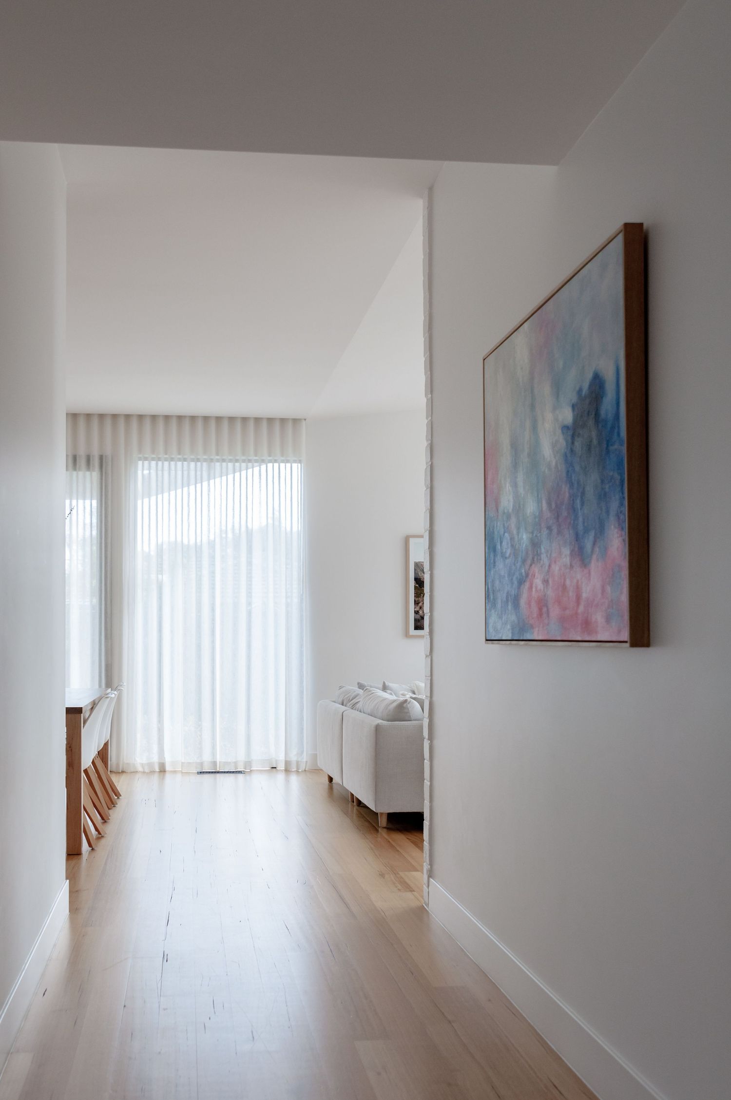 Bright hallway with wooden flooring, white walls, and abstract blue and pink artwork.