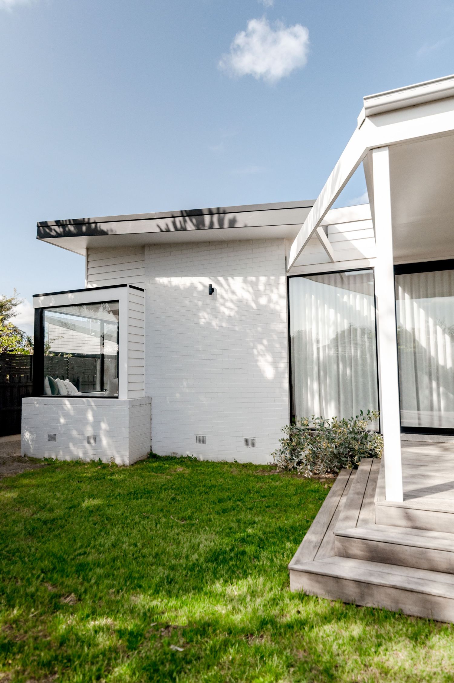 Modern white exterior of house with angular roof design and glass windows overlooking green lawn.