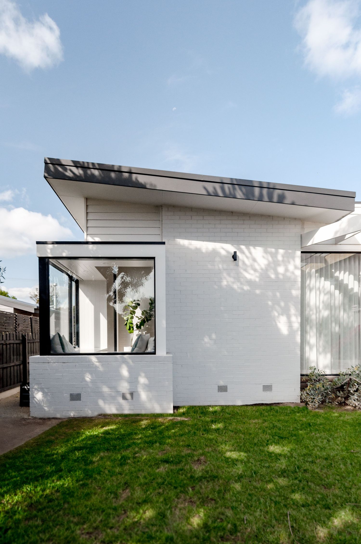 Contemporary white brick house with large corner window and angular roofline against blue sky.
