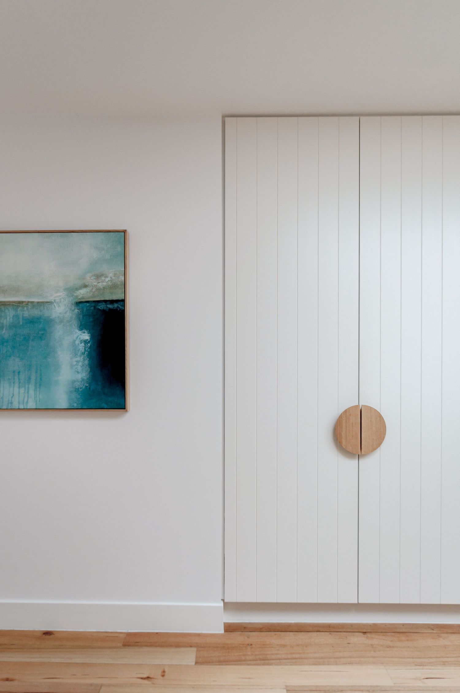 Minimalist interior featuring white paneled doors with round wooden handle and blue abstract artwork.