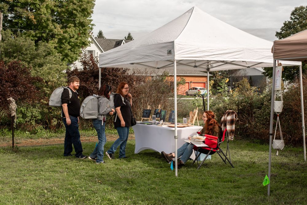 People gathered under a white canopy tent at an outdoor market or fair.