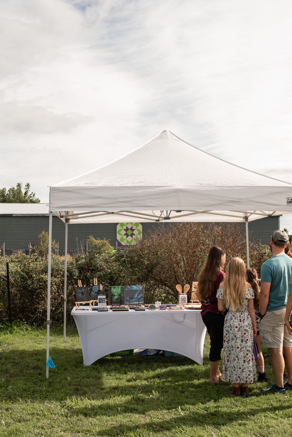 White canopy tent with display table set up on grassy area outdoors.