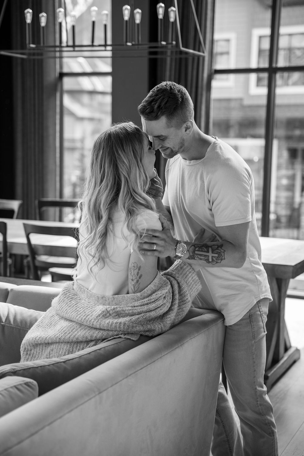 Black and white photo of couple cuddling on couch in romantic indoor setting.
