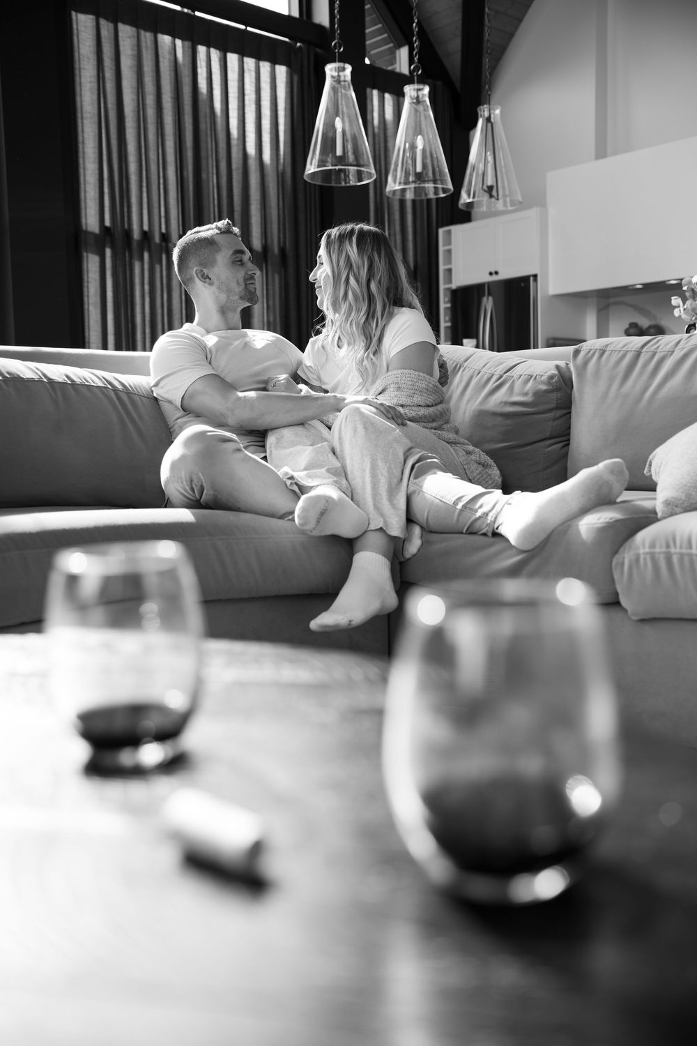 Black and white photo series showing people relaxing on a couch with wine glasses on a coffee table in the foreground.