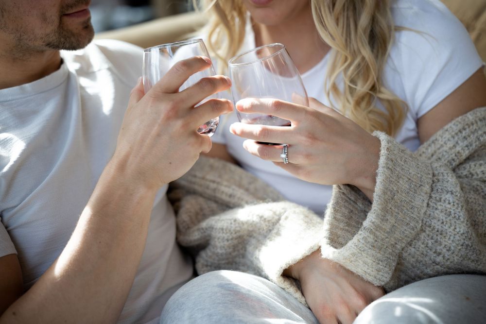 Two people share an intimate moment while holding coffee mugs and sitting close together on a couch.