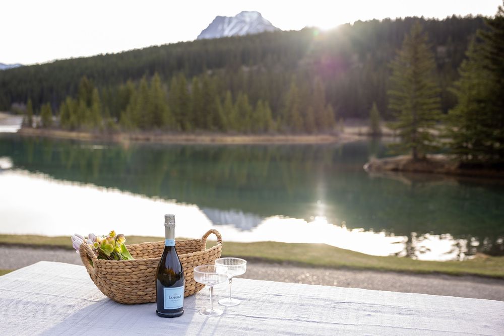 Mountain lake view with evergreen forest and snowy peaks reflecting in calm waters at sunset.