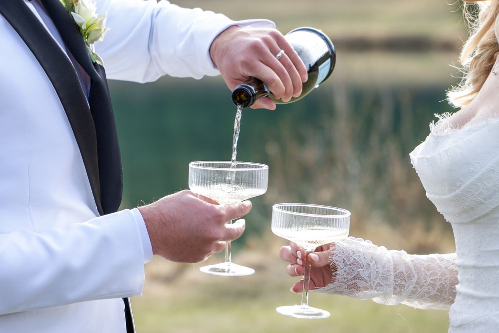 Newlyweds toasting with champagne glasses during an outdoor wedding celebration.
