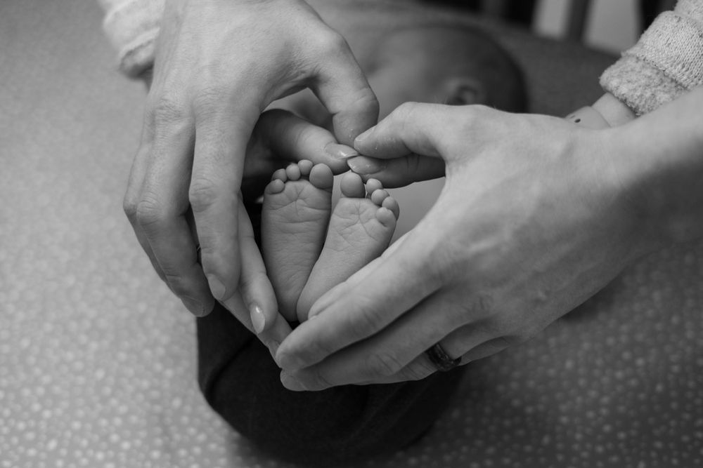 Caring hands cradle tiny baby feet in an intimate black and white portrait.