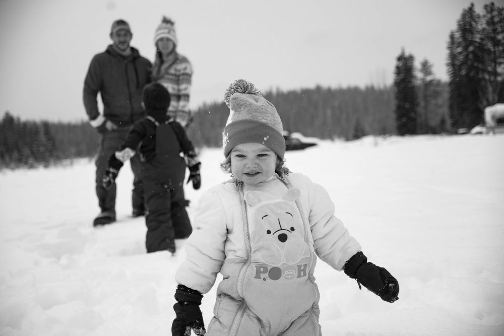 Child bundled up in winter gear walking through snow with family in background.