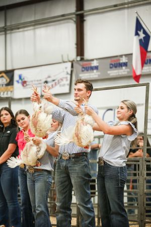 Contestants hold chickens in the air during a livestock competition event.