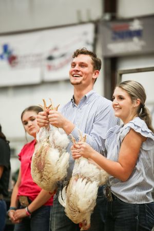 Competitors laugh while holding chickens during a fun livestock competition.
