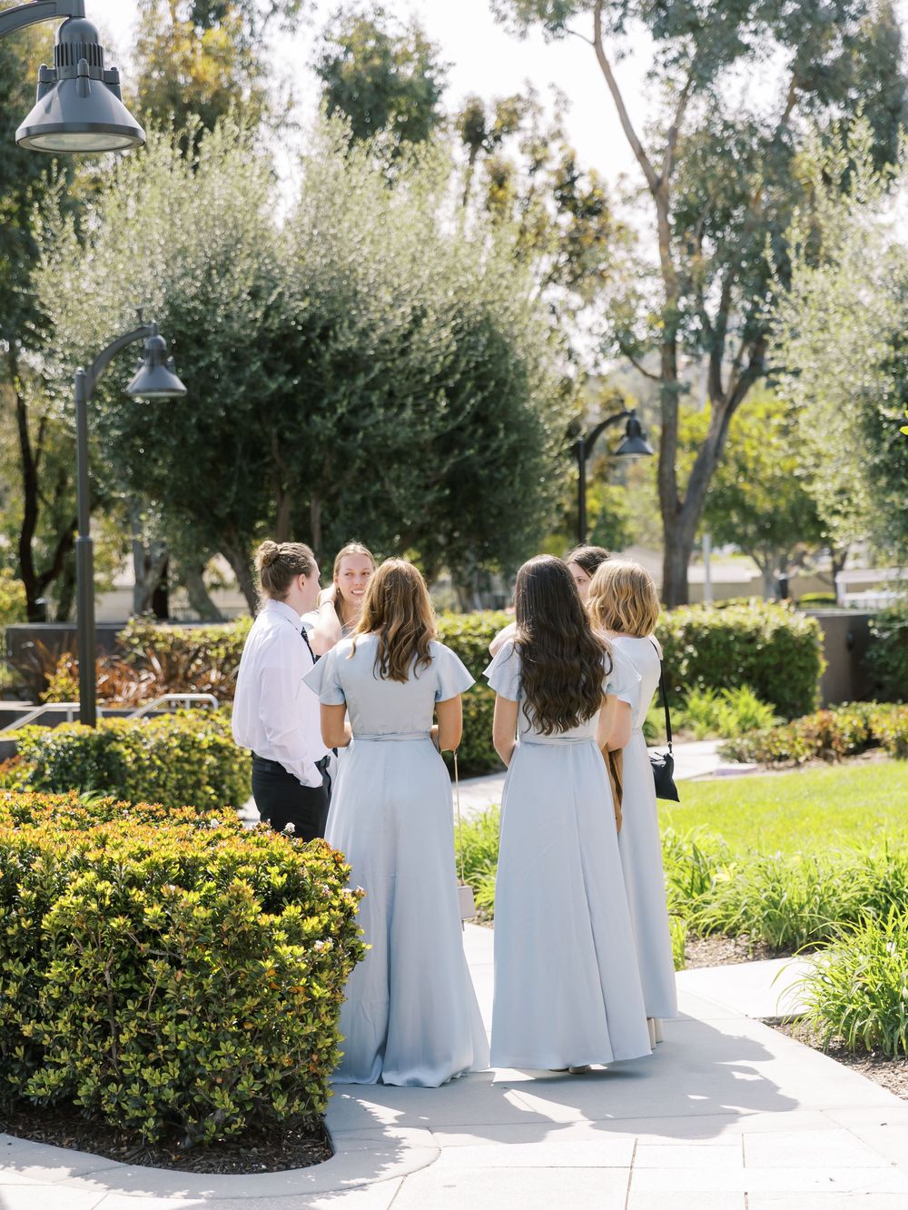 Wedding party walking along garden path in light blue and white attire.