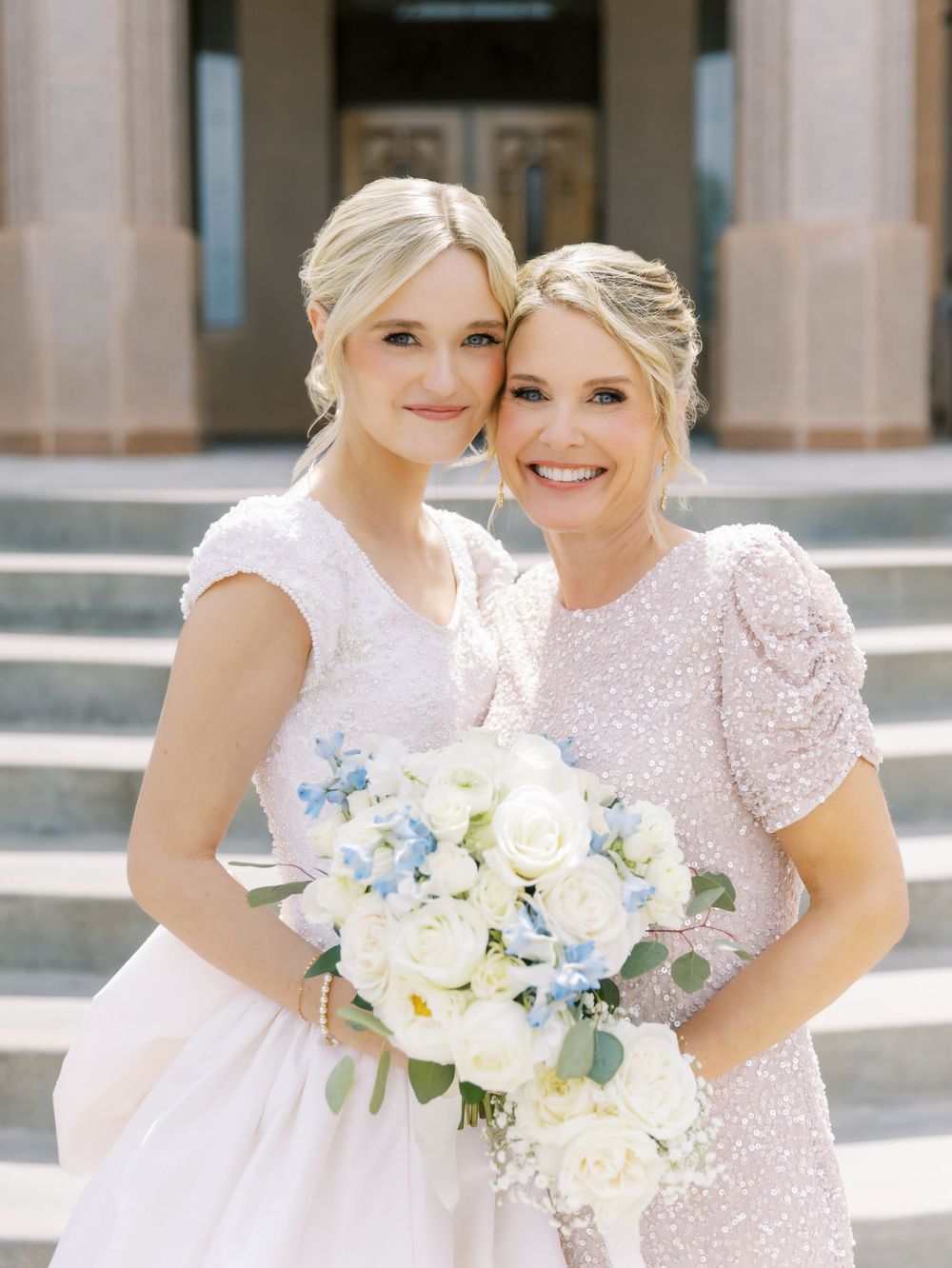 Bridesmaids in sparkly pink dresses holding white and blue floral bouquets.