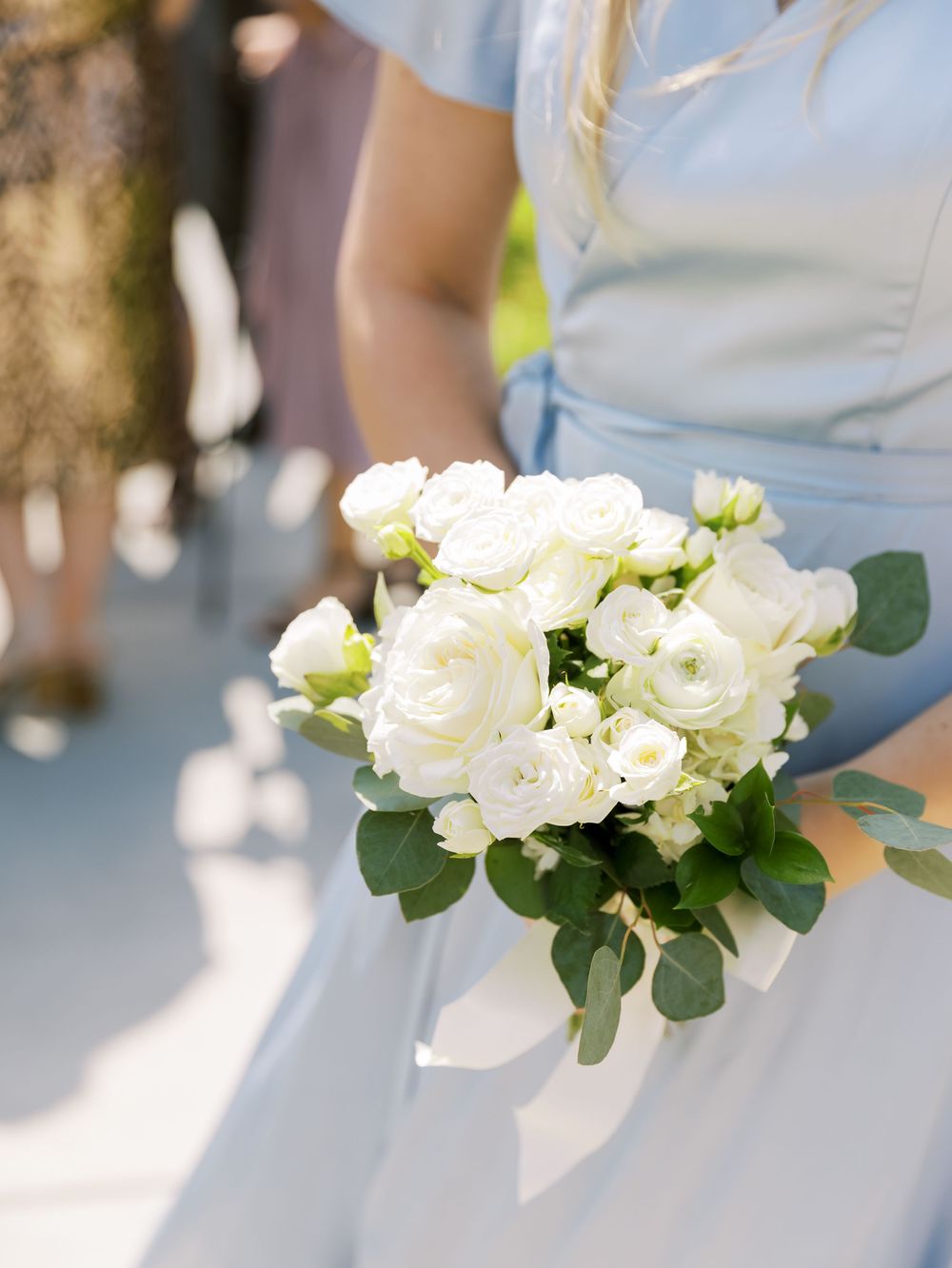 Elegant white wedding bouquet with roses and greenery held against a light background.