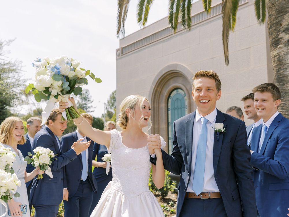 Wedding party poses outdoors in light blue and navy attire against garden backdrop.