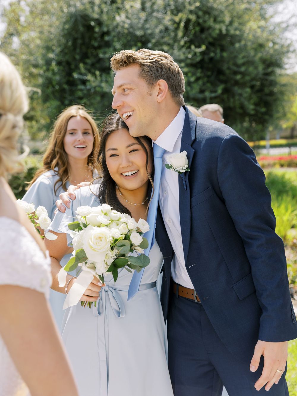 Wedding party members in blue dresses and navy suits sharing joyful moments outdoors.