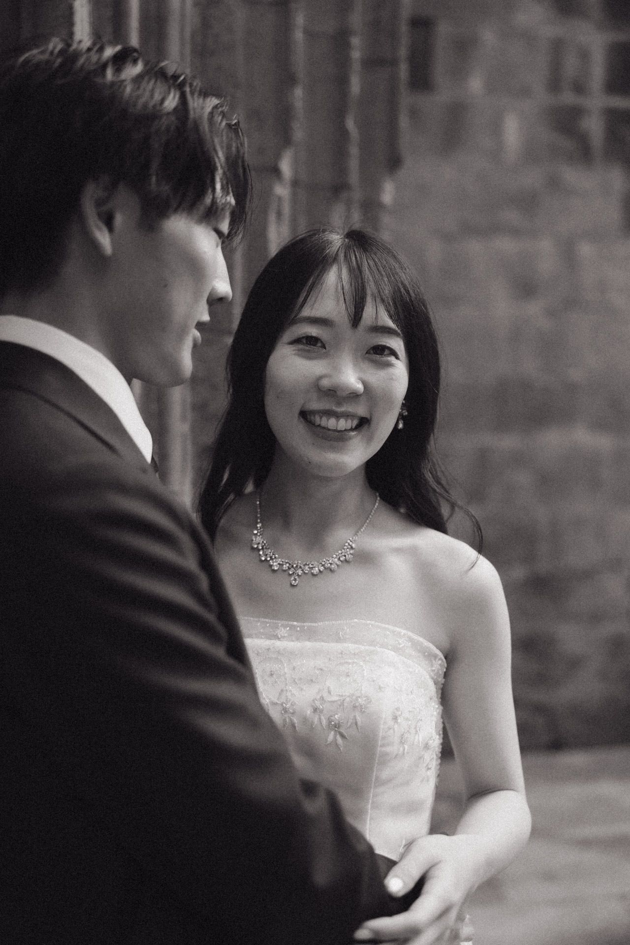 A black and white wedding photo showing a couple sharing a tender moment, with the bride wearing a strapless dress and necklace.