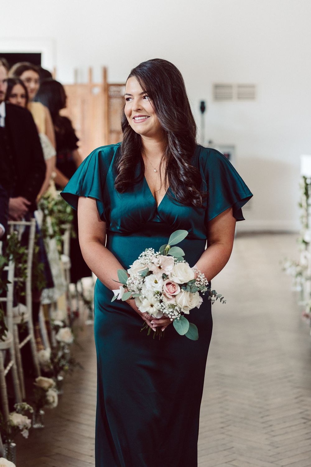 Bridesmaid in elegant teal dress holds a delicate white and blush floral bouquet with eucalyptus leaves.