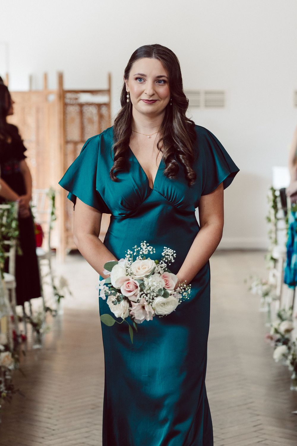 Person in teal dress holds delicate floral bouquet while standing in elegant venue hallway.