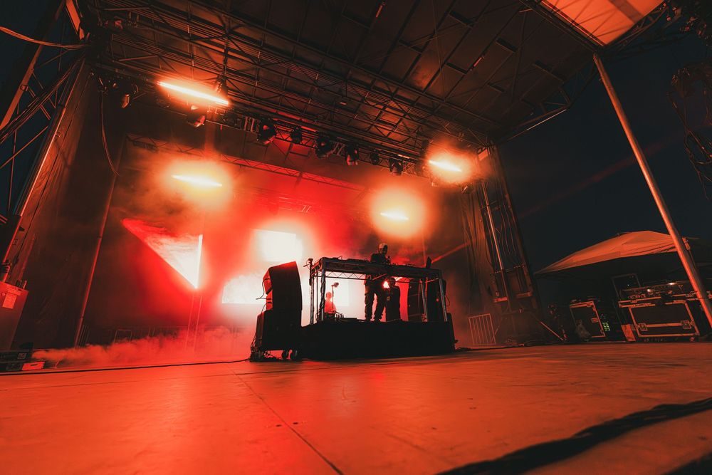Red stage lighting illuminates a dark performance space with dramatic shadows and angular architectural details.