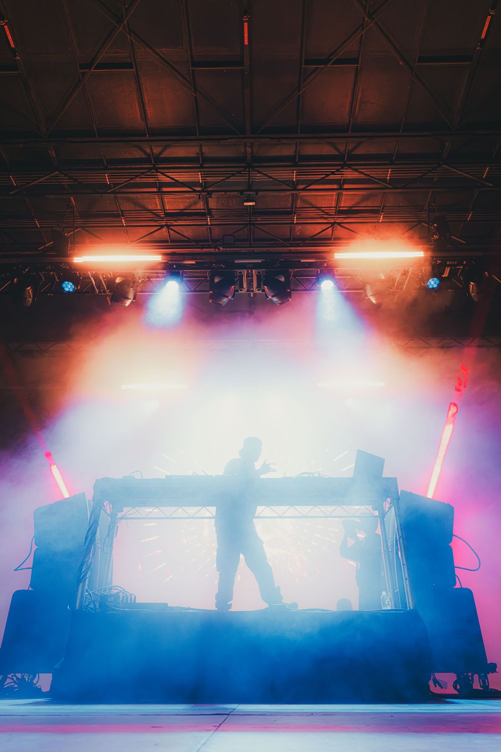 Concert stage lighting setup with dramatic red and blue atmospheric effects creating silhouettes against a smoky backdrop.