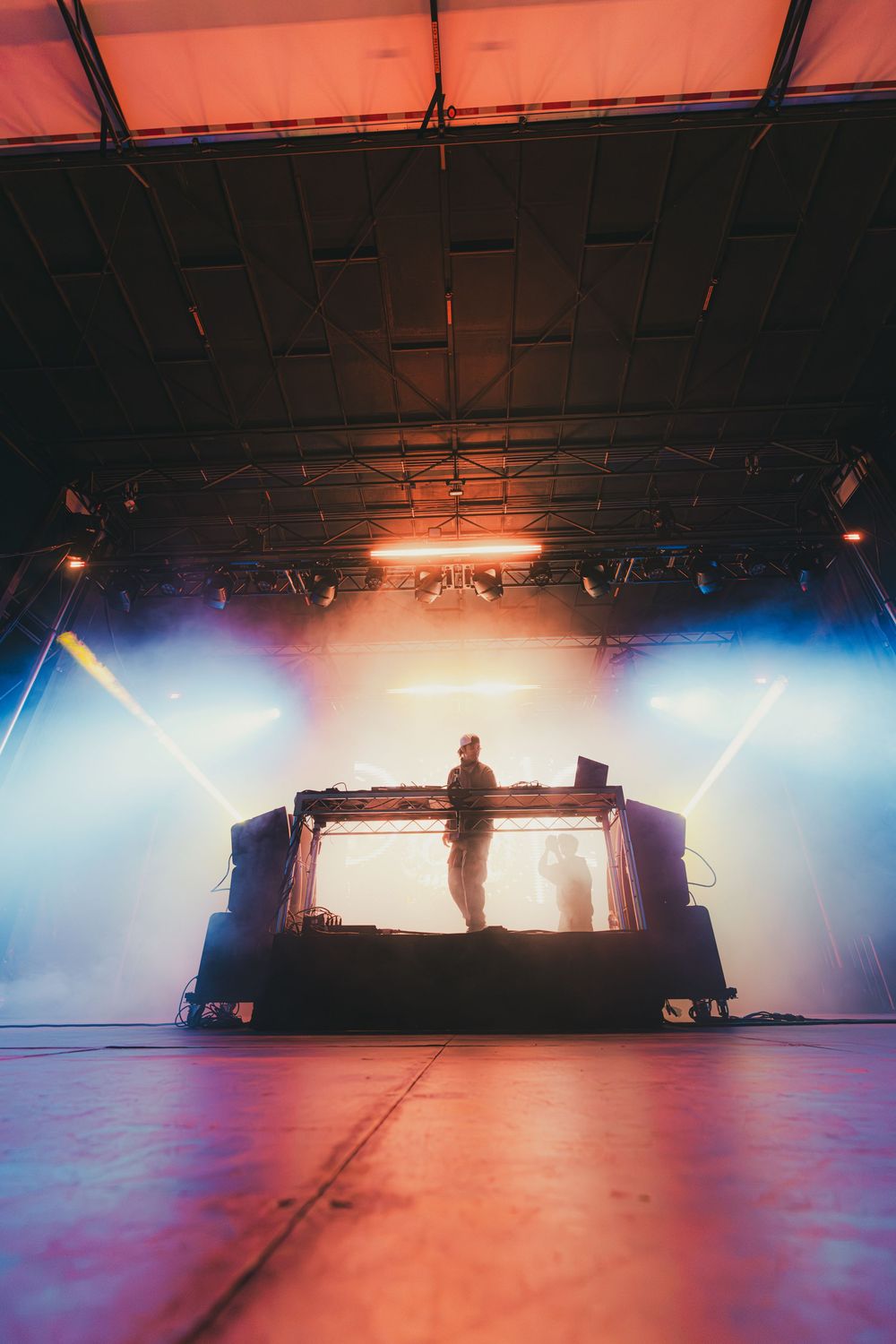 Silhouetted DJ booth on stage with dramatic blue and red lighting creating an atmospheric concert environment.