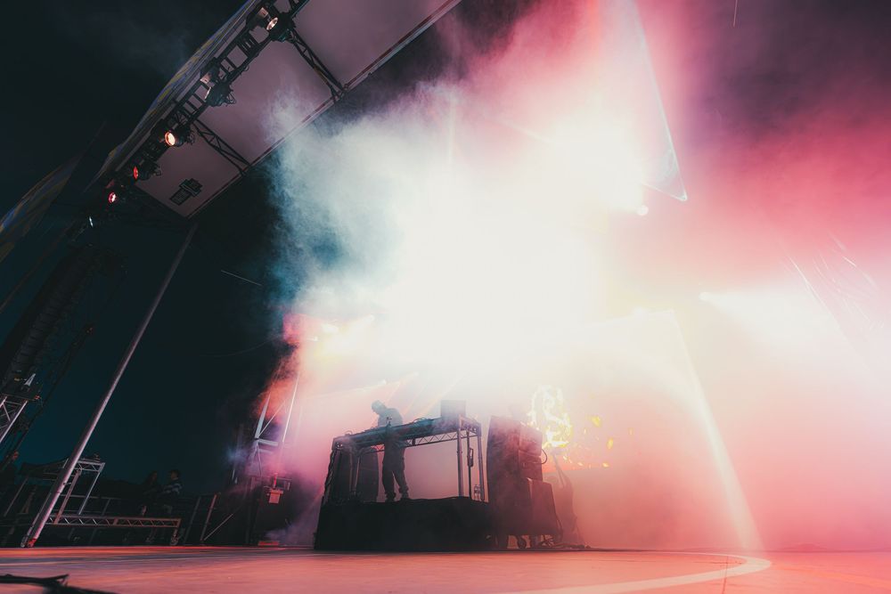 Dramatic concert stage lighting creates a moody atmosphere with pink and white fog effects during a live performance.
