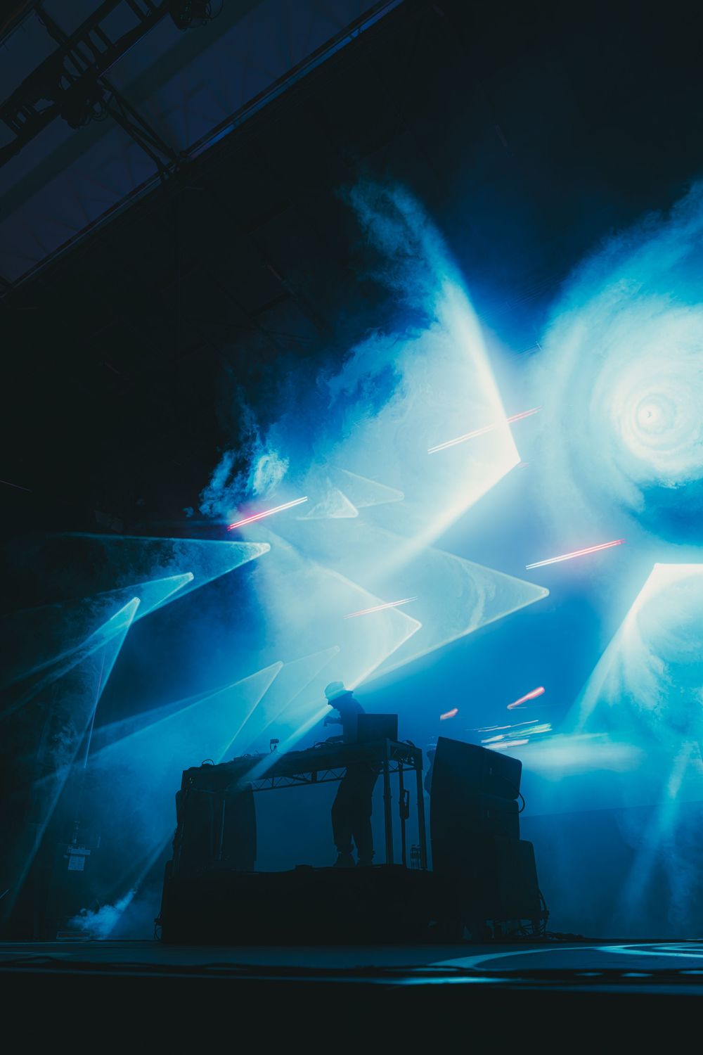 Dramatic sequence of blue spotlights illuminating a dark stage with silhouetted structures creating an atmospheric scene.