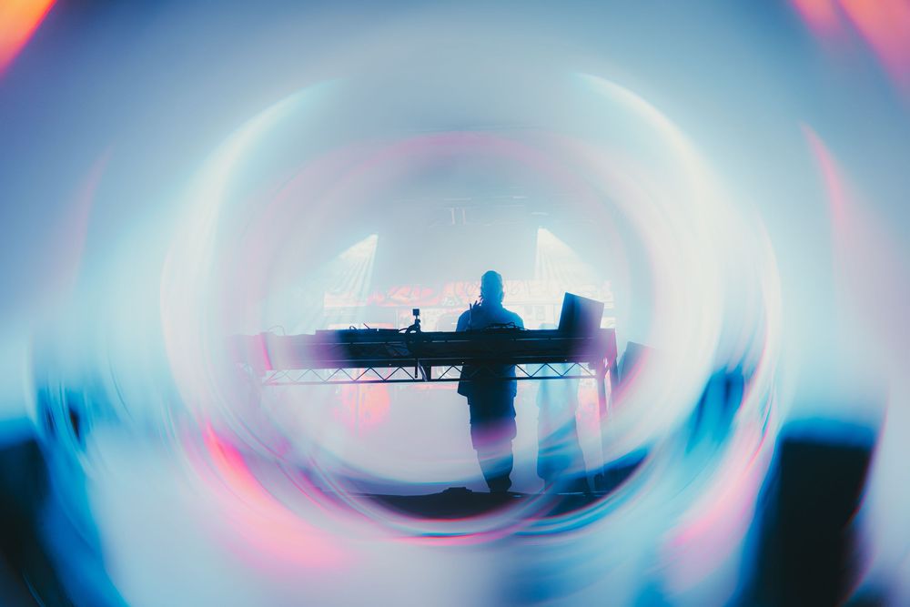 Abstract circular light patterns in pink and blue create a mesmerizing tunnel effect with silhouettes in the distance.