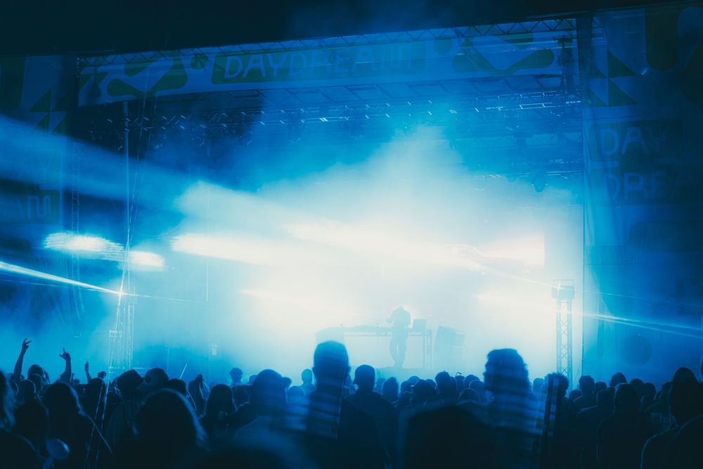 Concert crowd silhouettes raise their hands during a live performance under dramatic blue stage lighting.
