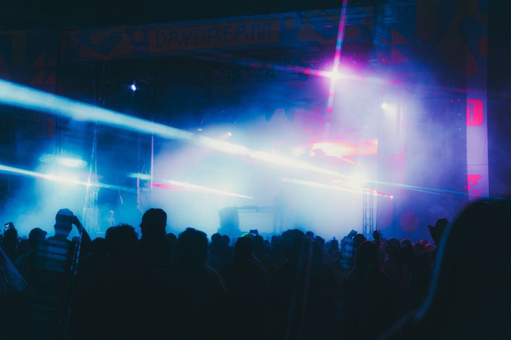 Concert crowd silhouettes dance under vibrant blue and purple stage lights at a nightclub event.
