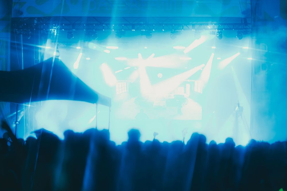 Bright blue light beams shine through dark silhouettes creating an atmospheric concert or performance venue setting.