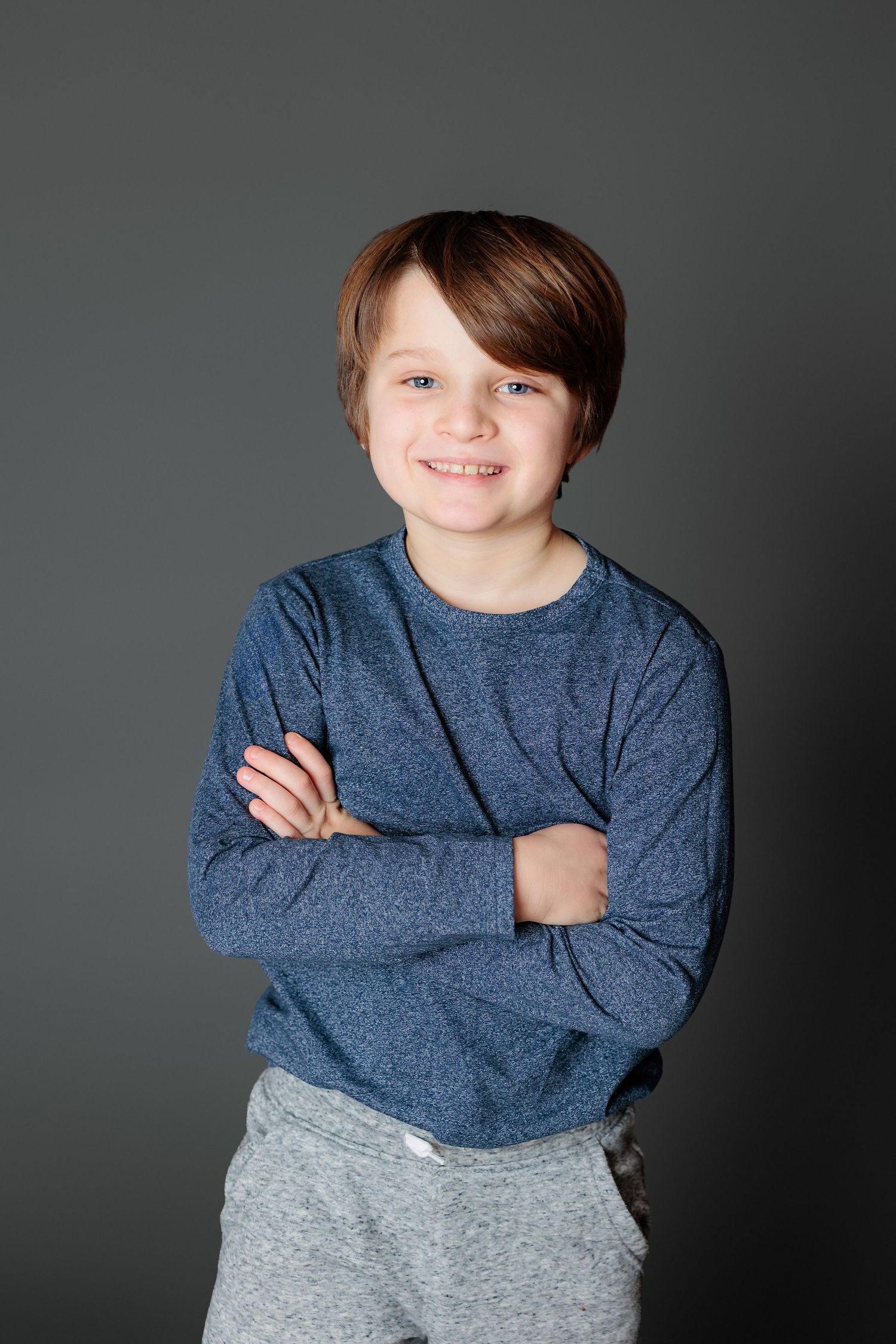 Child in blue sweater and gray pants poses against dark background in three sequential studio portraits.