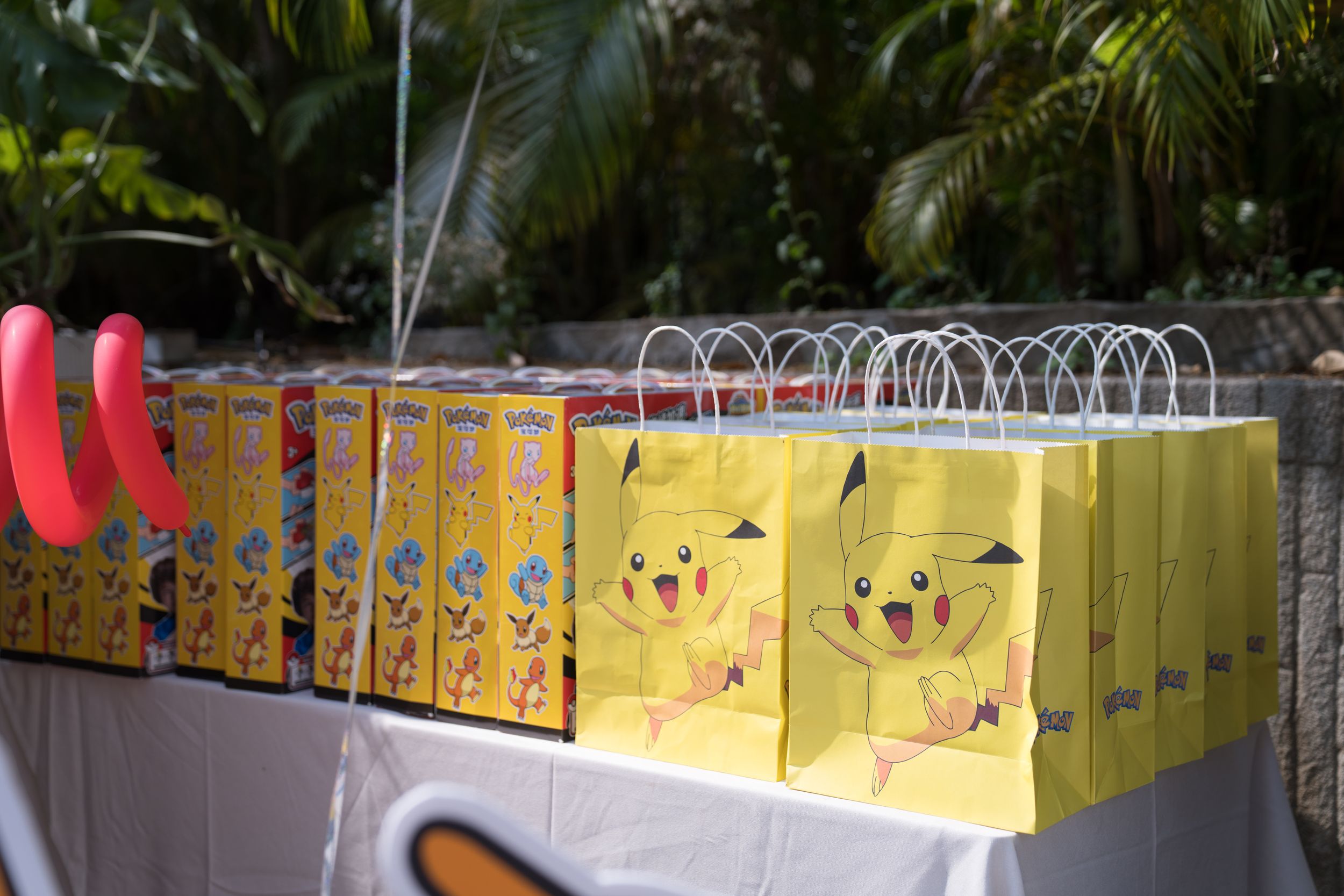 Yellow Pikachu Pokemon party favor bags lined up on a table at an outdoor birthday party celebration.戶外生日派對上，桌上擺放著一排黃色皮卡丘寶可夢主題的派對禮物袋。