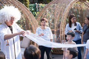 Students in white lab coats gather around woven dome structures during an outdoor educational activity.身穿白色實驗服的學生們聚集在編織圓頂結構周圍，參與戶外教育活動。