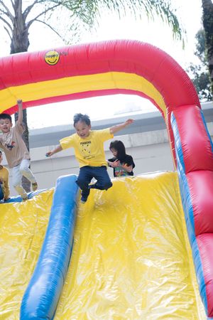 Kids having fun sliding down a large inflatable yellow and red bounce house slide at an outdoor event.孩子們在戶外活動中玩得不亦樂乎，他們正從一個大型的黃色和紅色充氣蹦床滑梯上滑