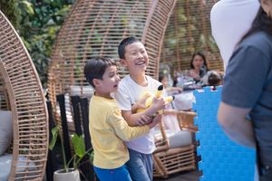 A group of people gather outdoors around woven rattan hanging chairs on a sunny day在陽光明媚的日子裡，一群人聚集在戶外，圍坐在藤編吊椅旁。