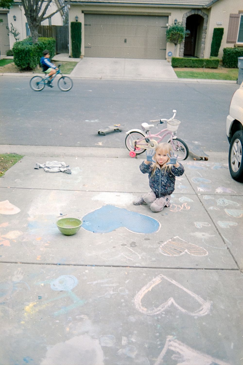 Colorful chalk art and drawings decorate a concrete driveway as children play and create on a sunny day.