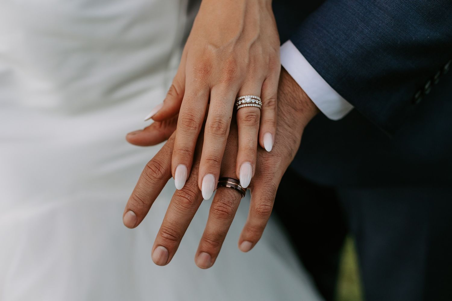 Newlywed couple displaying wedding rings on their hands, bride wearing white dress and groom in navy suit in La Jolla.