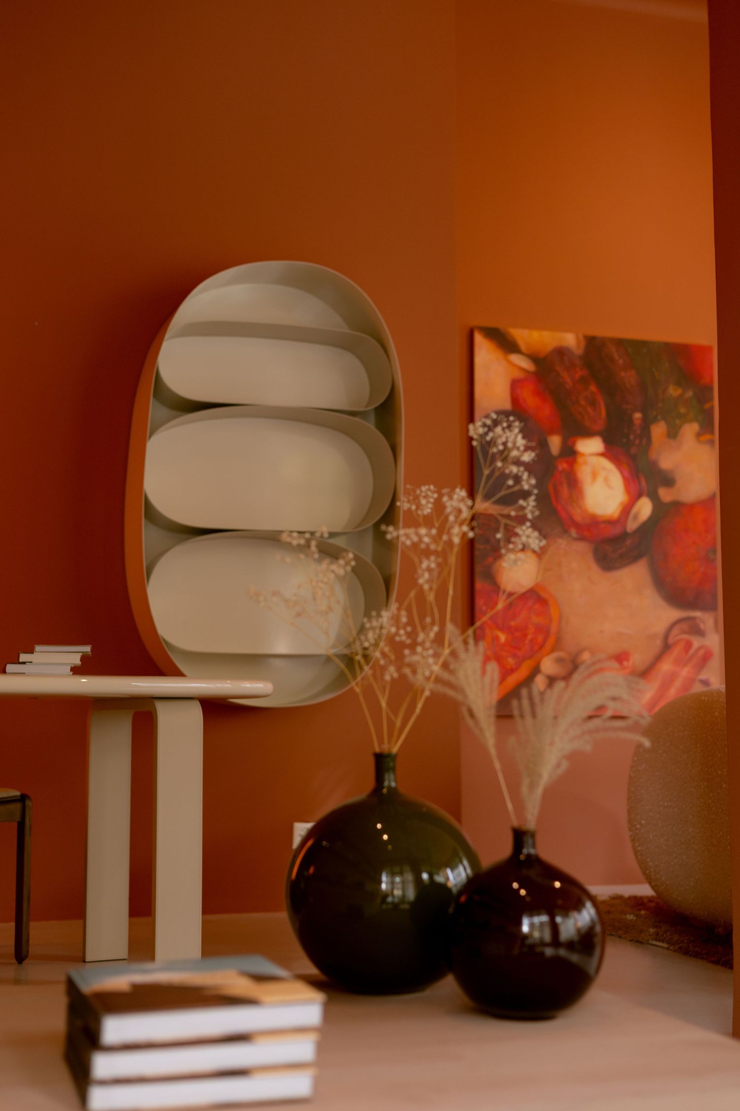 Modern dining room with olive green walls, wooden sideboard, four framed prints, large orange vase, and light blue chairs.