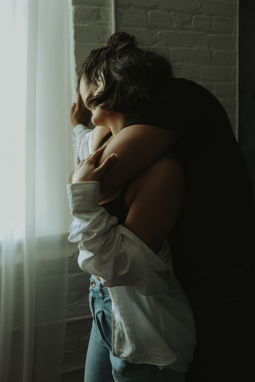 A series of four moody photographs showing a person in a white shirt and jeans against a brick wall in soft lighting.