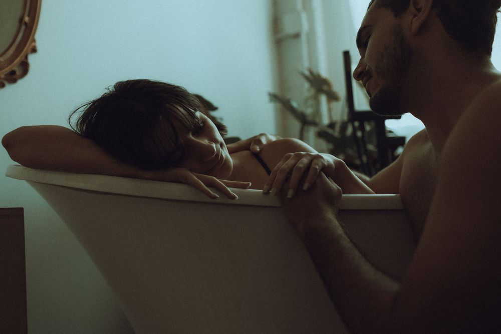 A tender intimate moment between two people in a dimly lit bathroom.